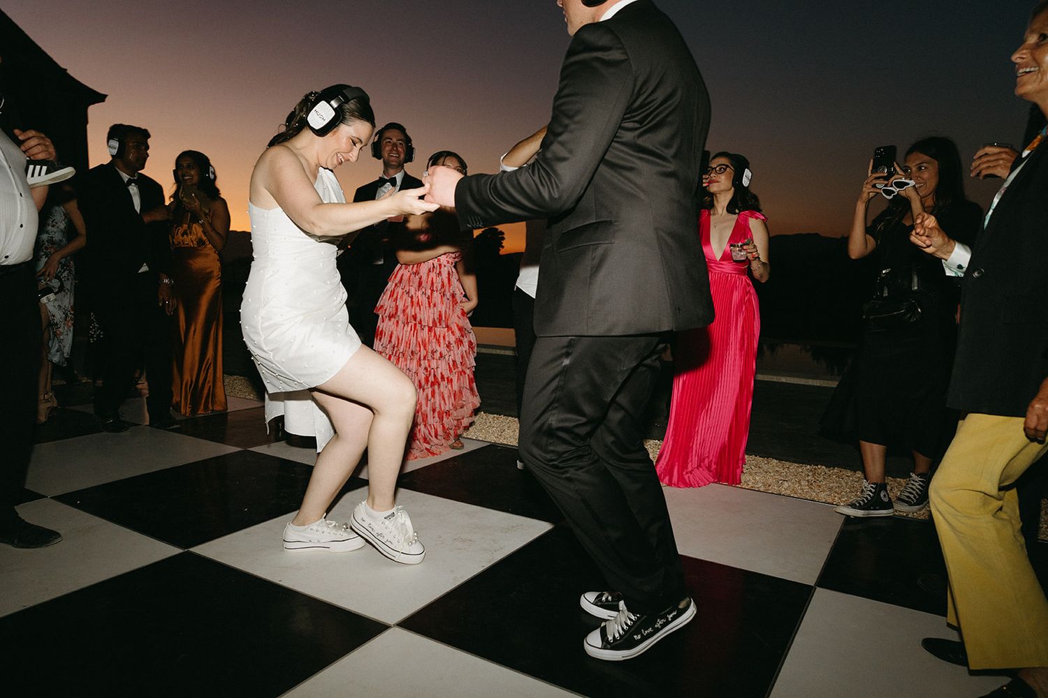 Couple dancing playfully at wedding reception on black and white checkered dance floor at sunset.