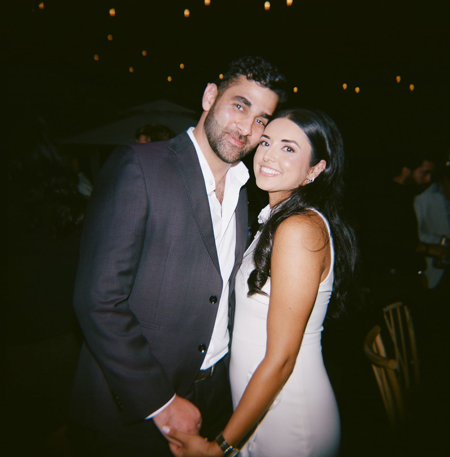 A romantic couple sharing an intimate moment at a dimly lit evening celebration.