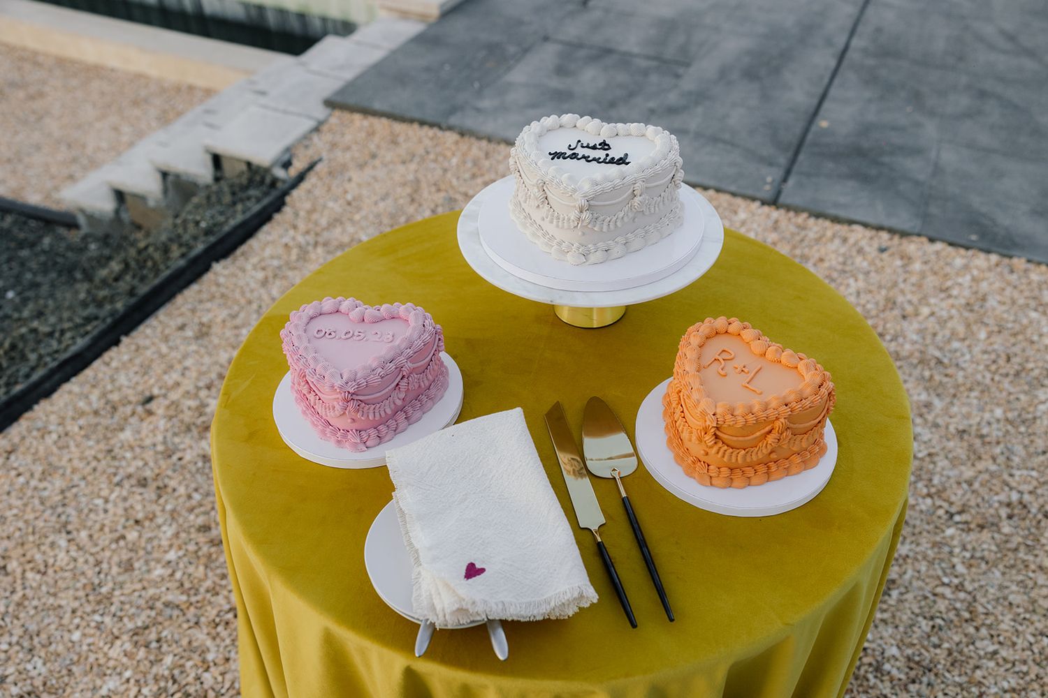 Three heart-shaped wedding cakes in white, pink and orange displayed on yellow tablecloth.