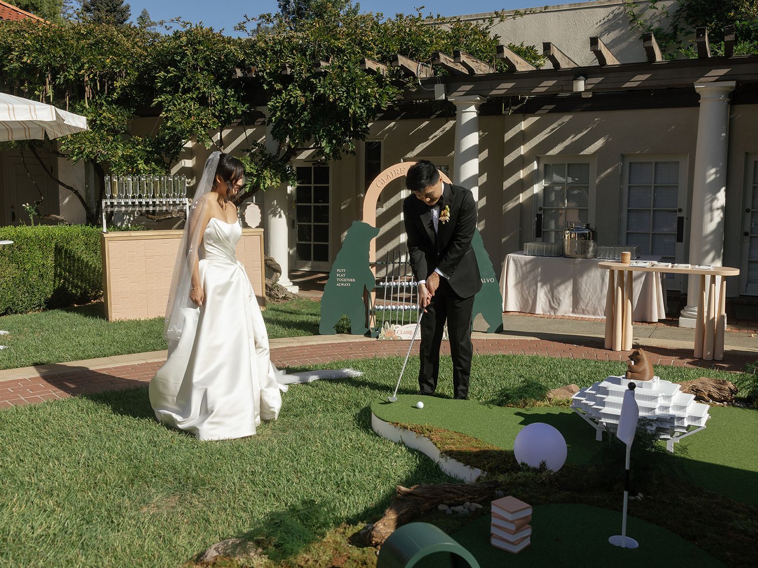 Bride and groom playing mini golf in a lush garden venue on their wedding day.