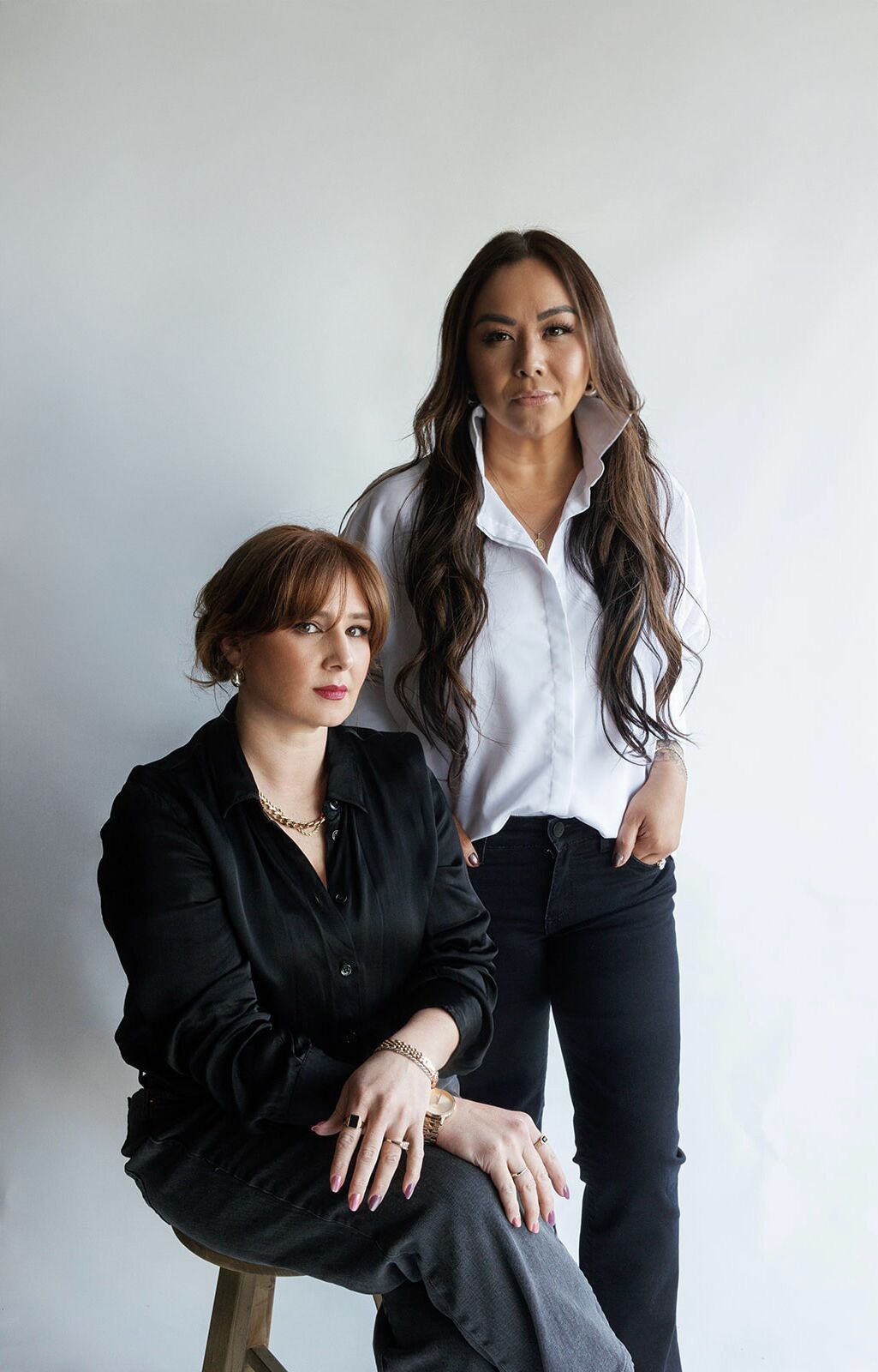 Two people in business attire pose together against a white backdrop in a professional studio setting.