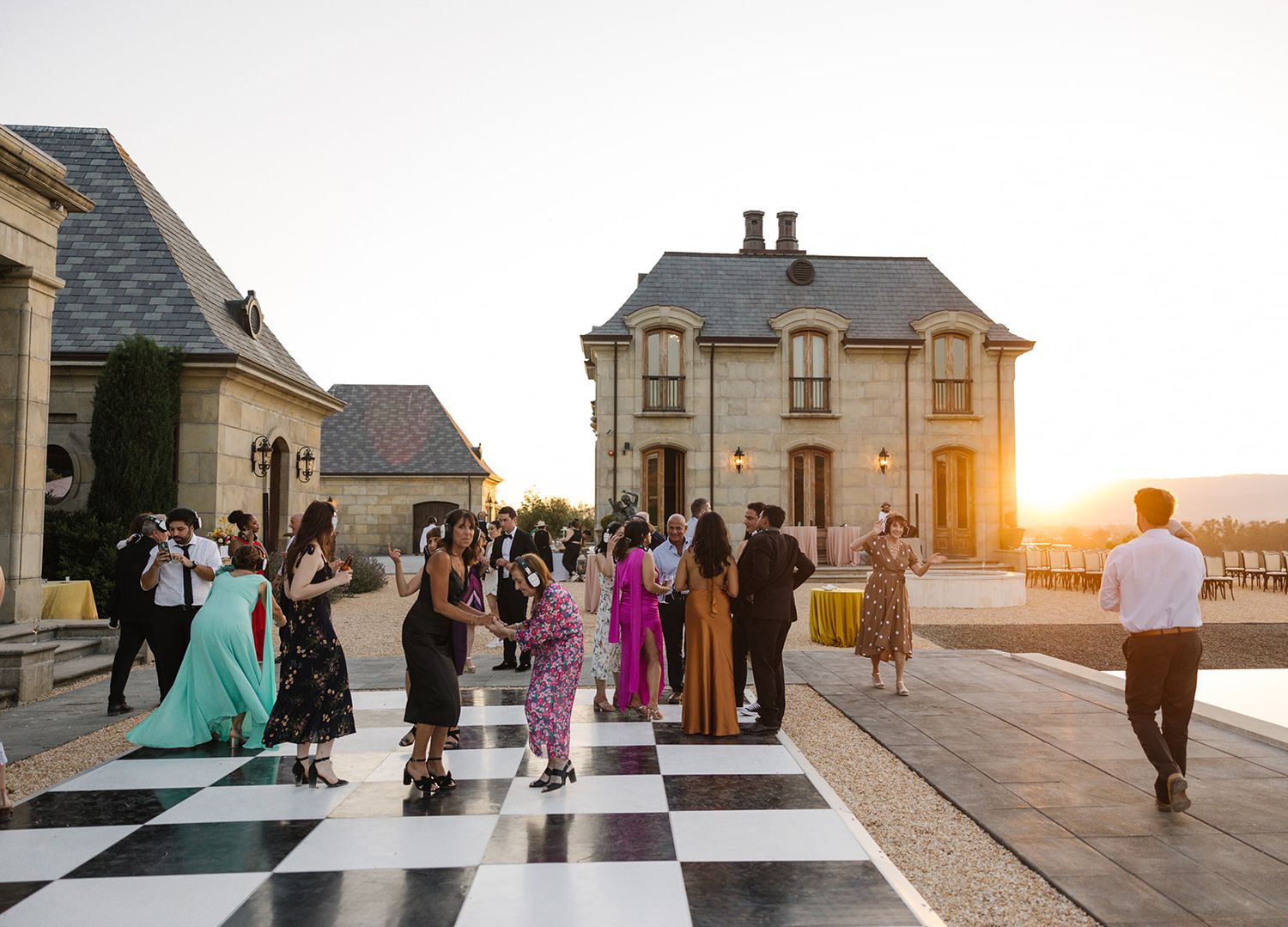 Wedding guests gathered on a black and white checkered dance floor at sunset.
