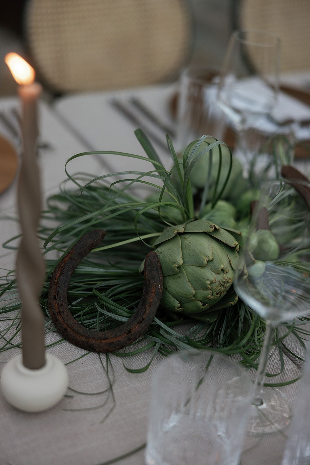 A rustic table setting features artichokes and air plants arranged with natural elements in muted green tones.