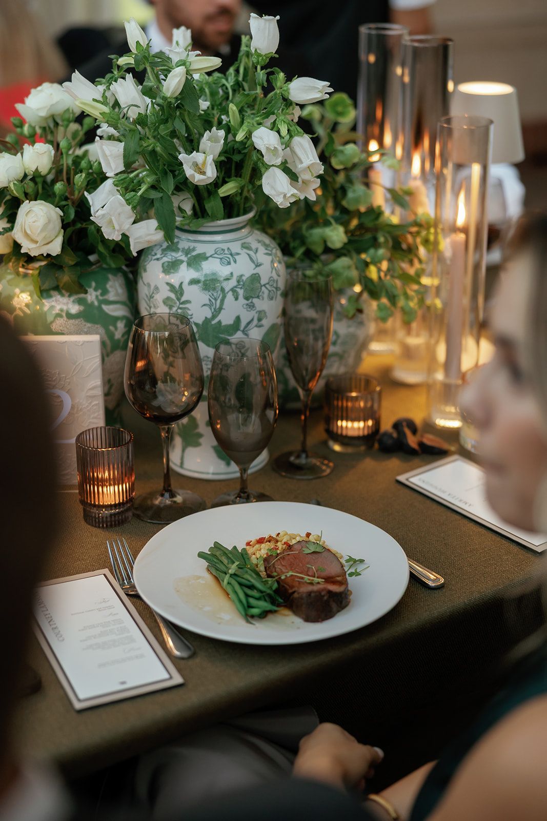 Close-up of wedding reception table setting with white floral centerpieces, candles, and plated dinner service.