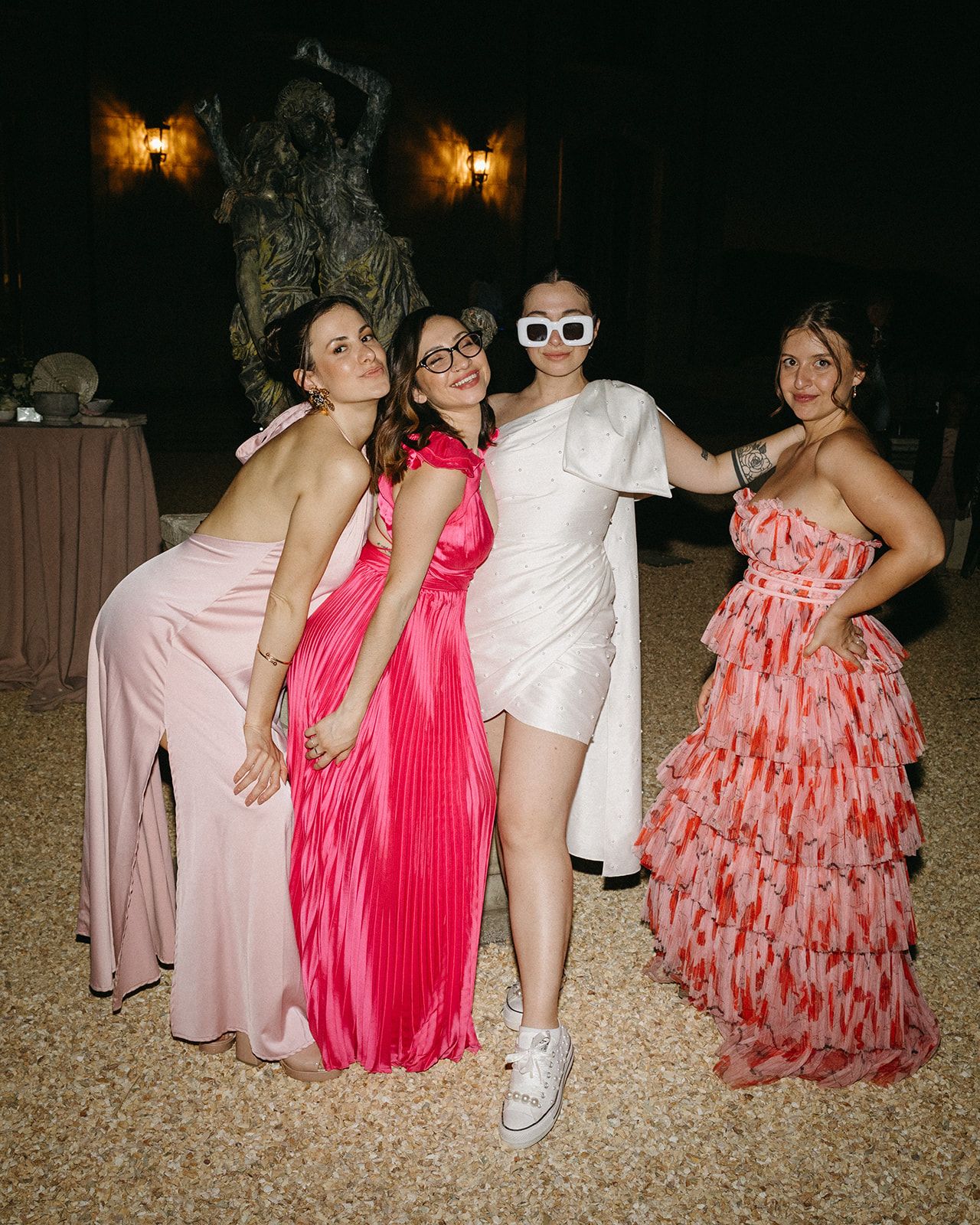 Group in colorful formal dresses striking fun poses at evening wedding reception.