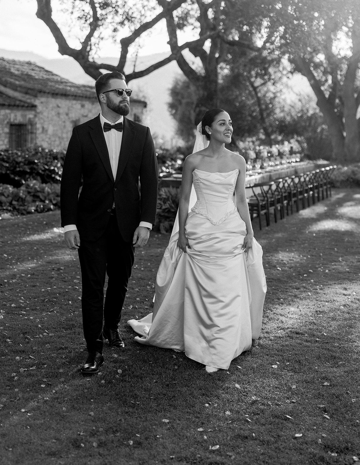 Wedding couple takes a romantic stroll along a tree-lined path in black and white.