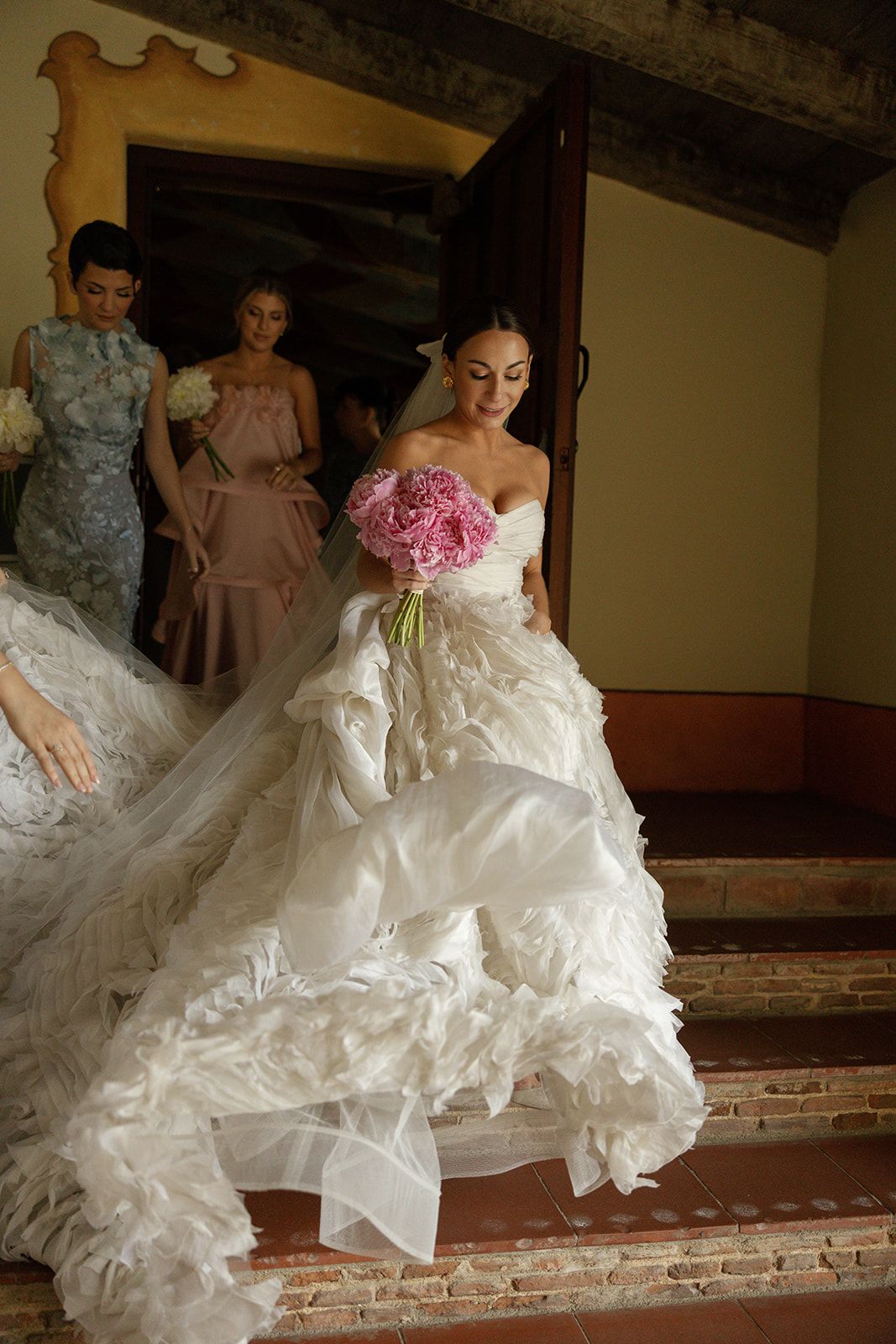 A sequence of photos showing the flowing layers of a white wedding dress as someone descends stairs with a pink bouquet.