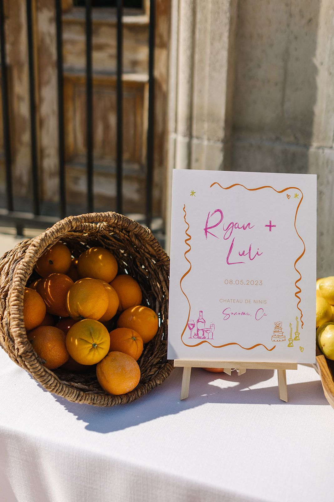Wedding sign display with basket of fresh oranges on white linen table.