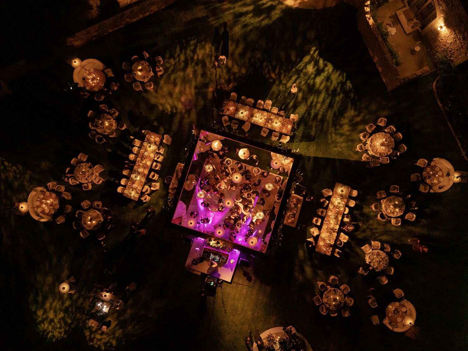 Aerial night view of wedding reception with glowing round tables and purple-lit dance floor.