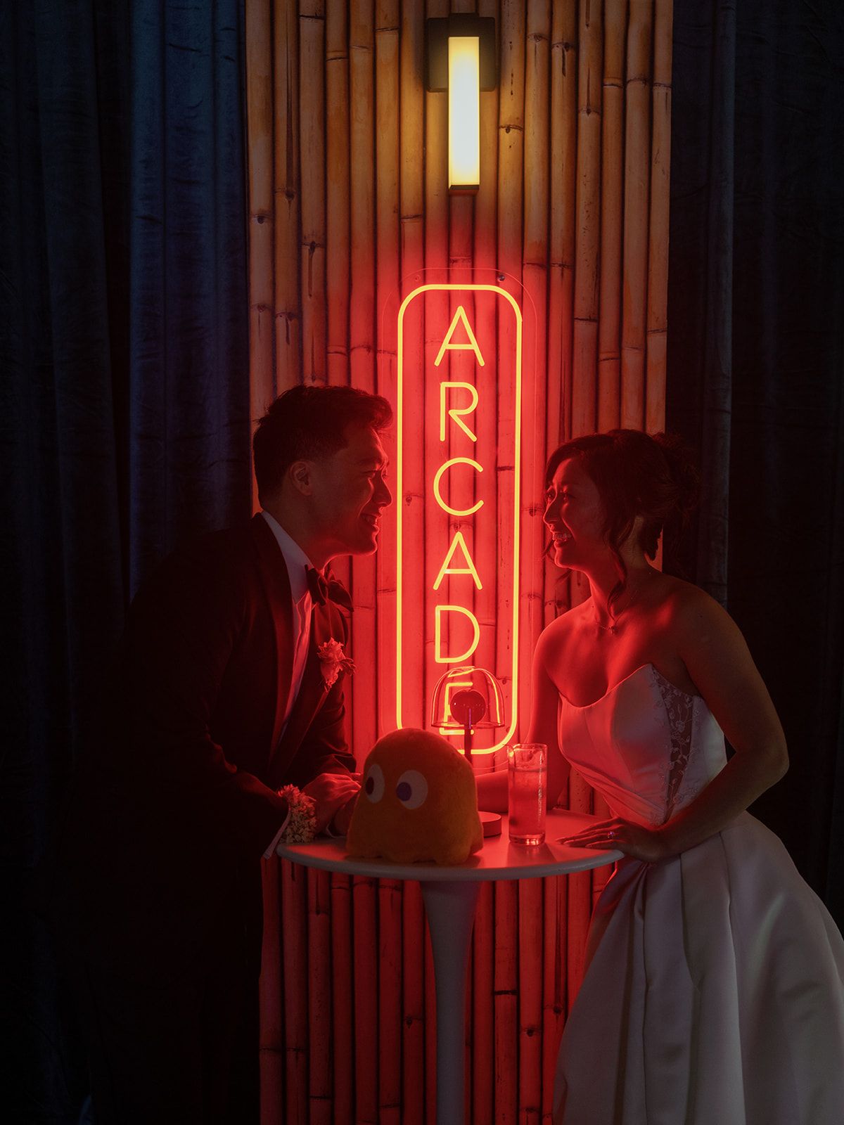 Bride and groom share a romantic moment beside a glowing red neon Arcade sign at their wedding reception.