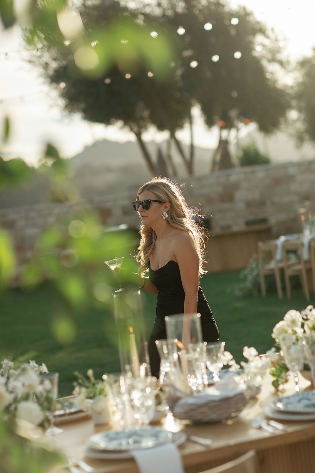 Elegant outdoor wedding reception table settings with string lights and white floral centerpieces at sunset.