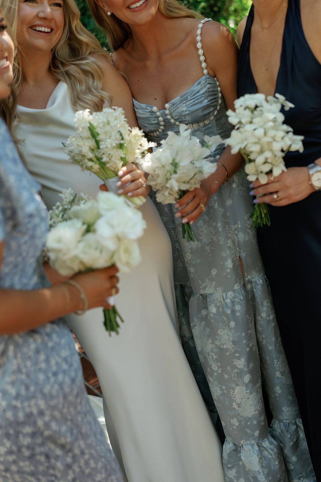 Bridesmaids in sparkly silver dresses stand with bride holding white rose bouquets at elegant wedding celebration.
