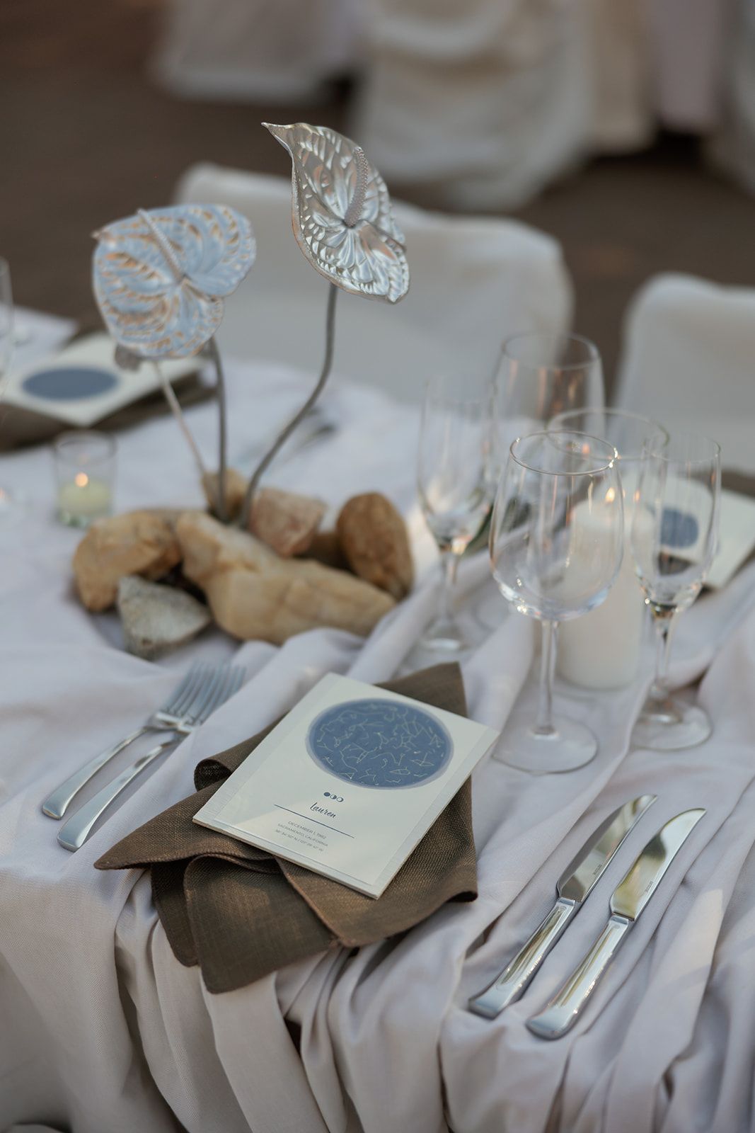 Elegant wedding table setting with white tablecloth, menu card, wine glasses, and decorative glass butterfly accents.