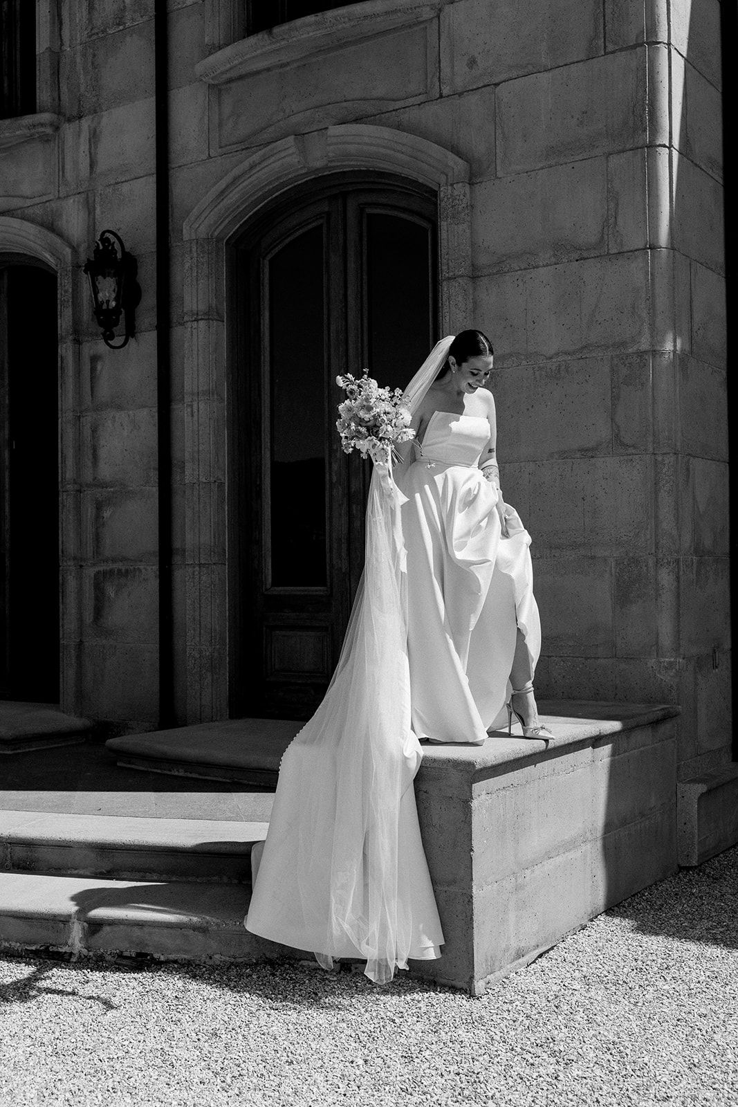 Four black and white photographs show a figure in a flowing white dress moving poetically against a stone wall in sunlight.