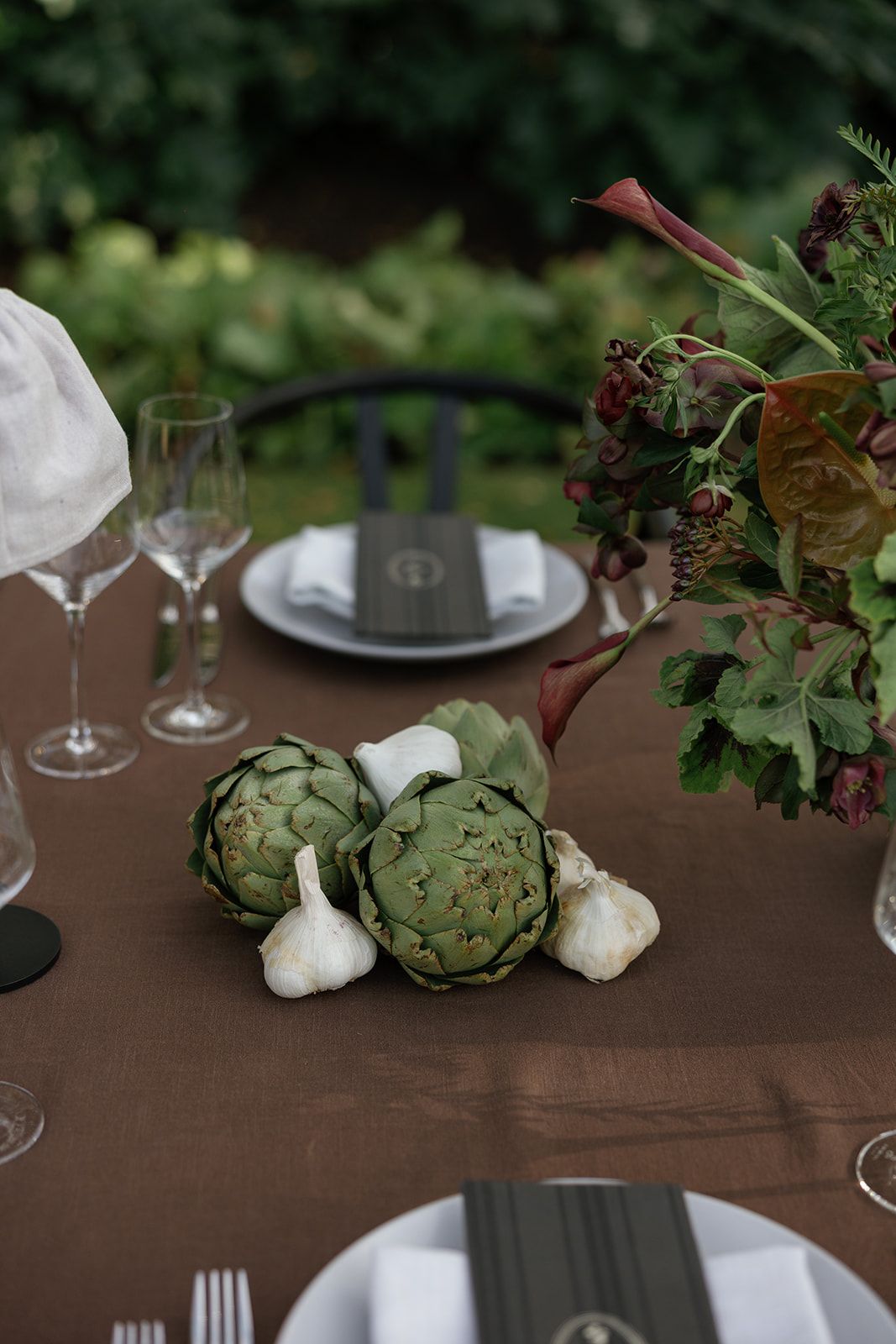 Rustic table setting with artichokes and garlic bulbs as natural decor elements against a dark wooden surface.