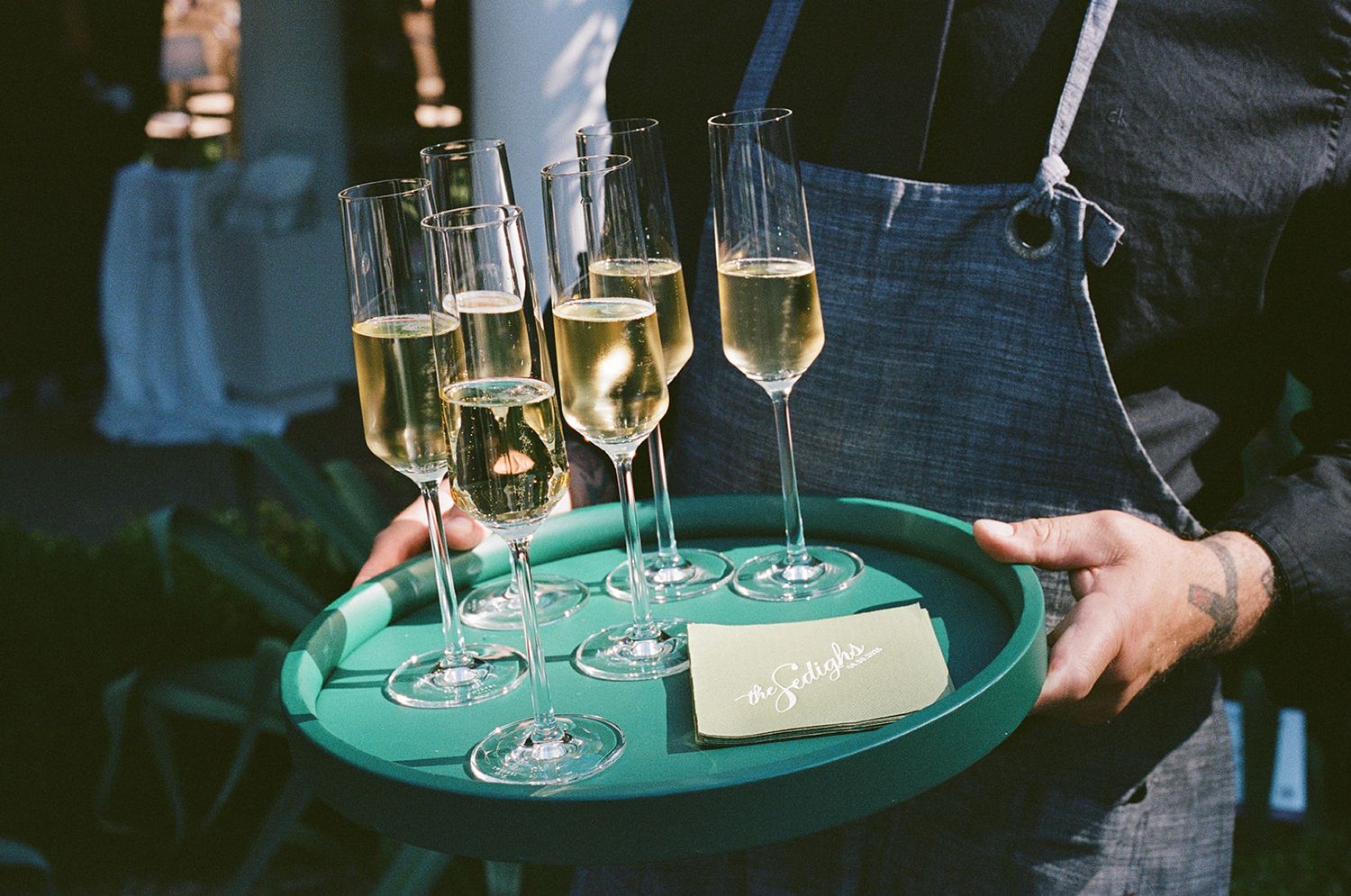Server carries tray of champagne glasses filled with sparkling wine at an elegant event.