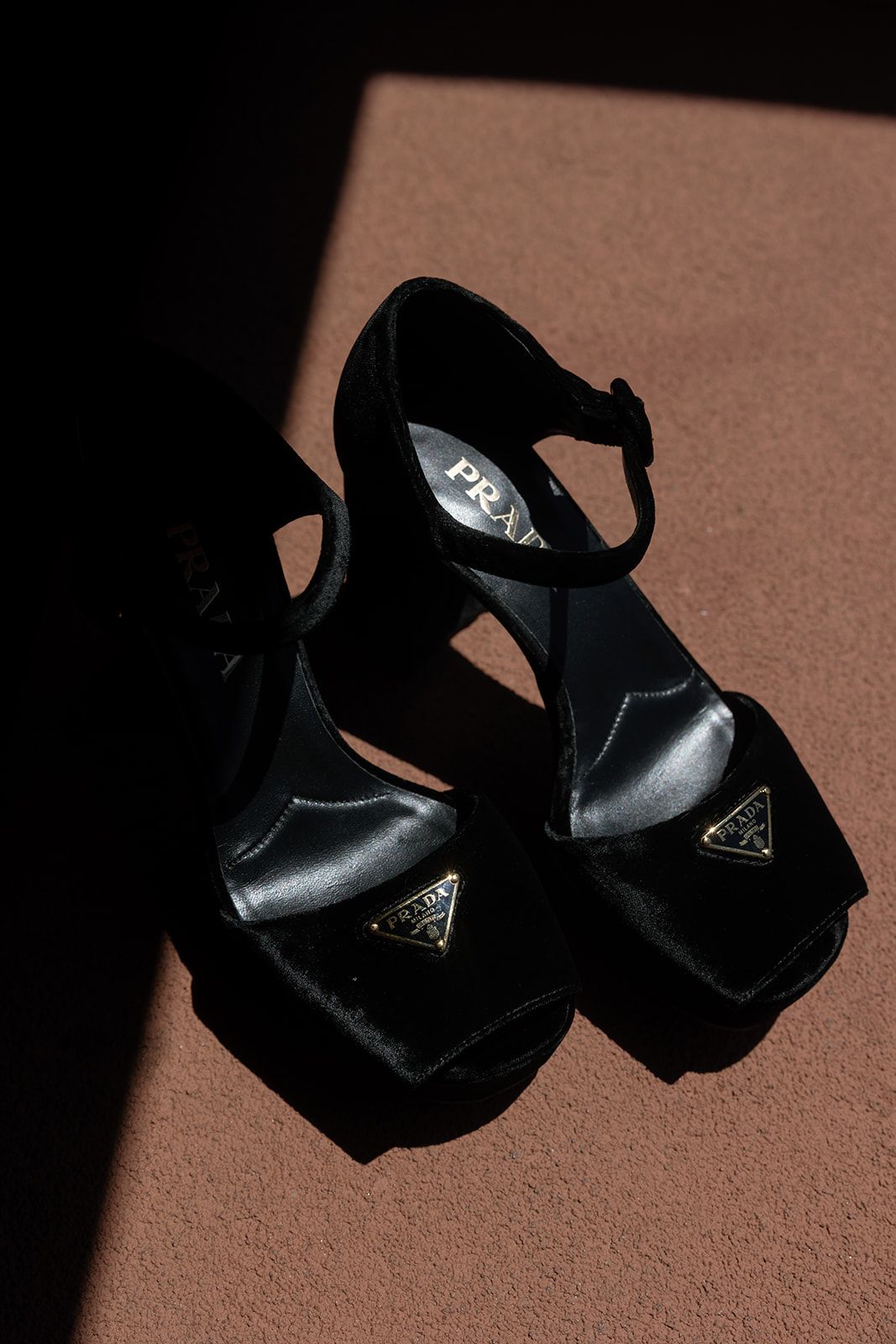 Close-up view of black platform sandals with metallic hardware details casting shadows on a tan background.