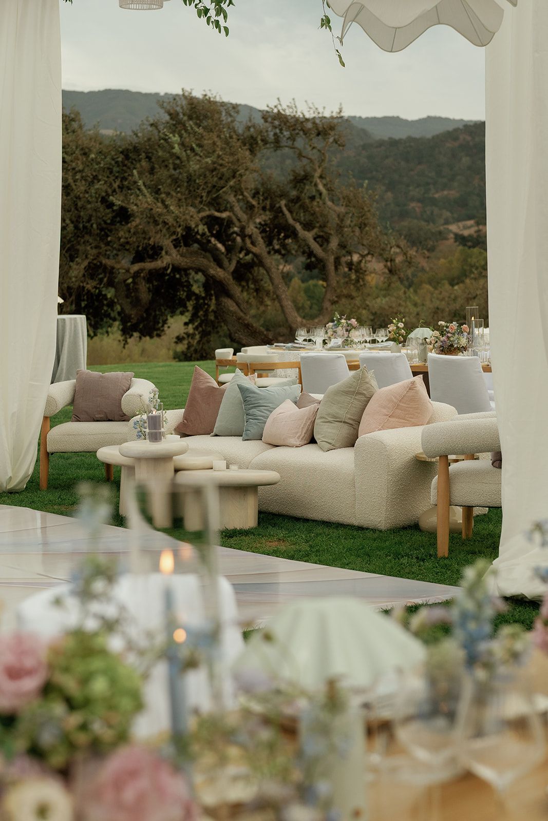 Elegant outdoor wedding lounge with cream sofas, colorful pillows, and scenic mountain views.