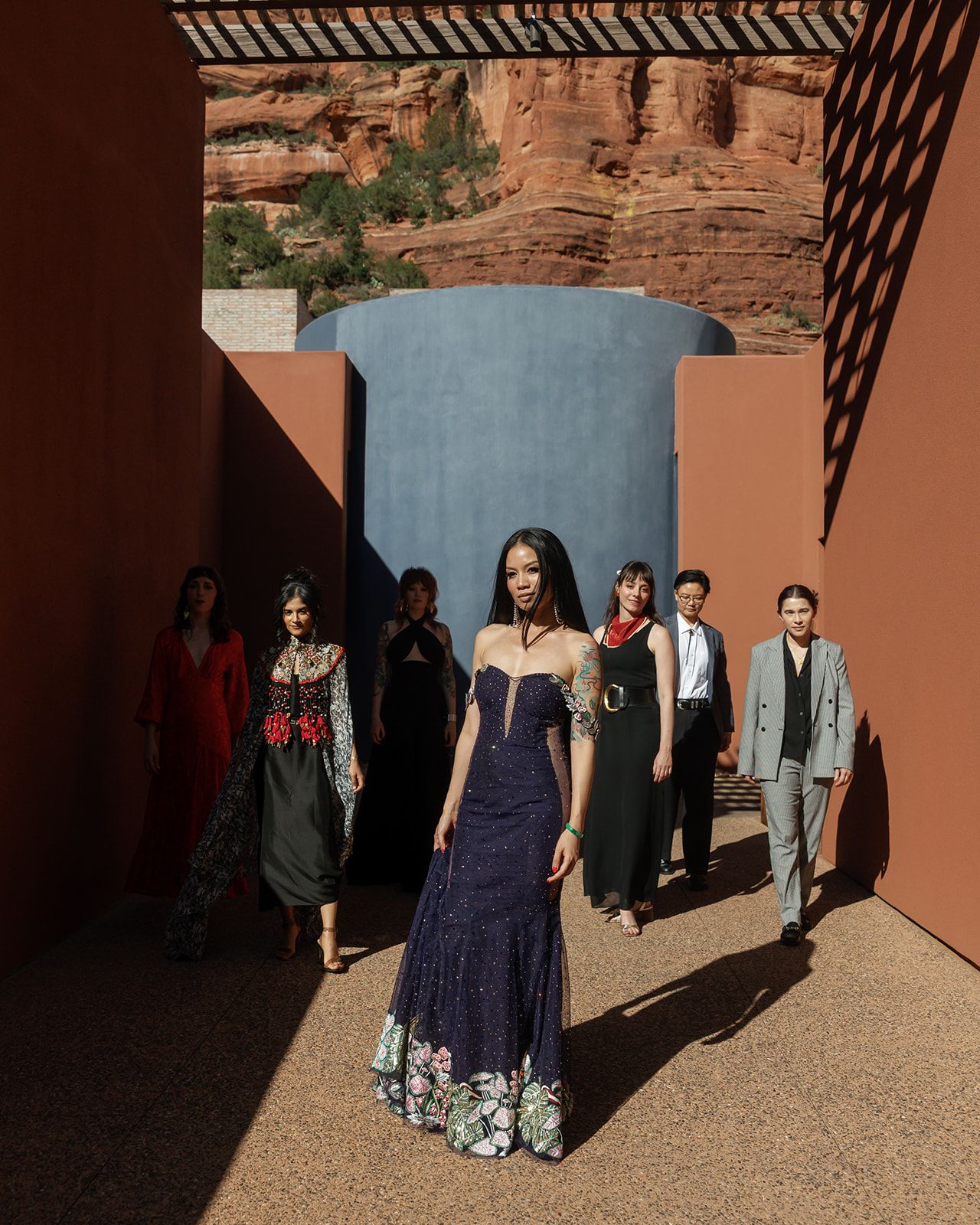 A group walks through an architectural space with red rock formations and stone walls in the background.