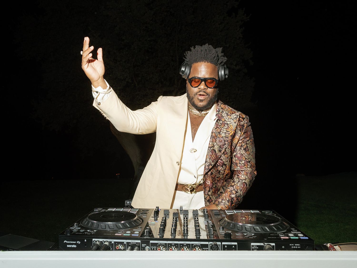 Stylish DJ performing at an outdoor event wearing sunglasses and a patterned blazer.