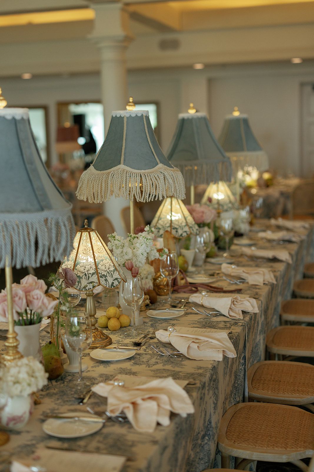 Elegant table setting with vintage fringe lamps, pink flowers and place settings at an upscale event venue.