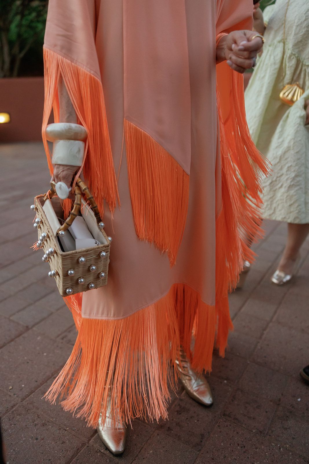Woman wearing a peach and orange fringe dress paired with metallic shoes and a studded handbag.