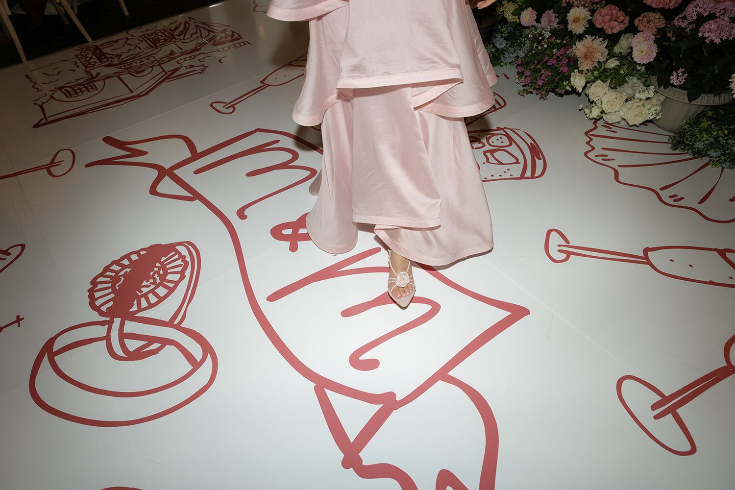 Pink clothing over a floor decorated with whimsical red line drawings at an event setting.