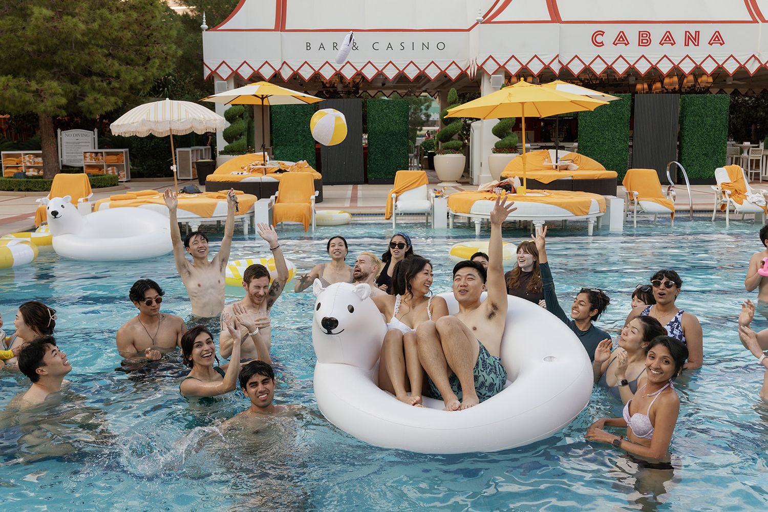 Group of friends enjoying a pool party at a resort casino, posing on a white polar bear float.