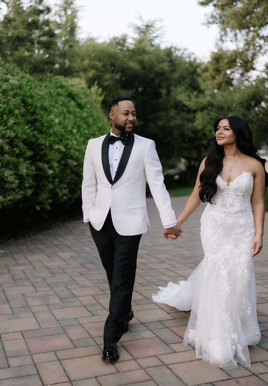 Elegant couple in formal wedding attire walking together on stone path.