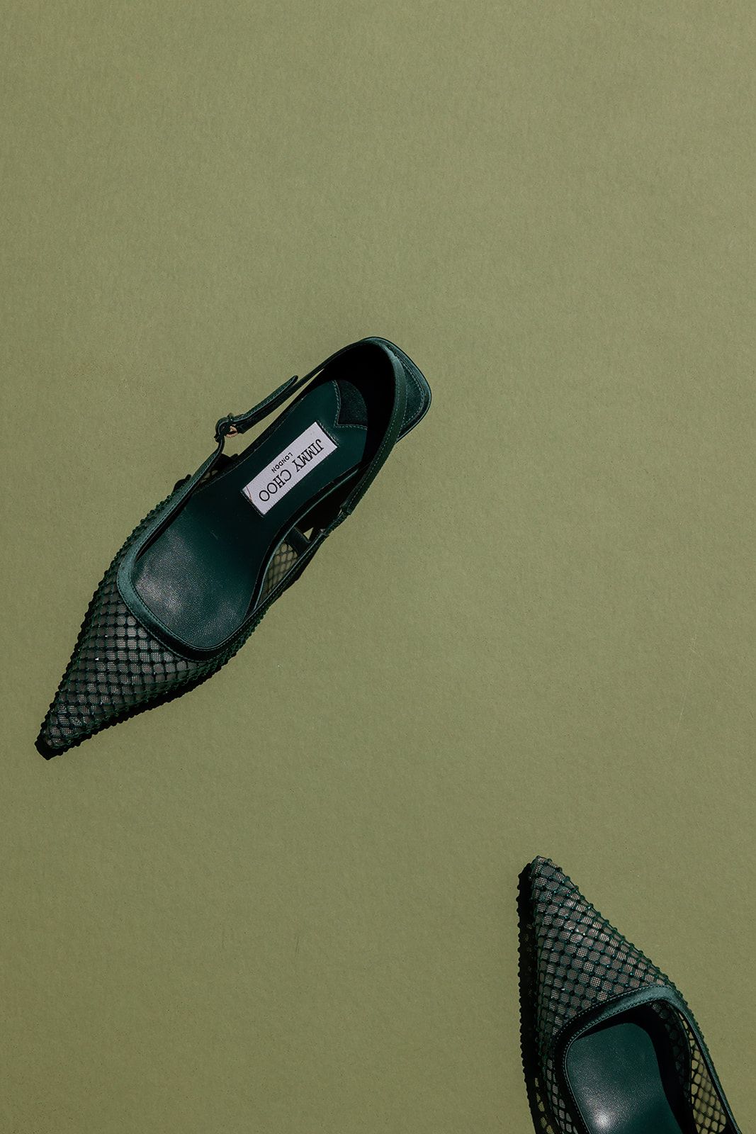 Two black textured leather pointed-toe flats on a sage green background.