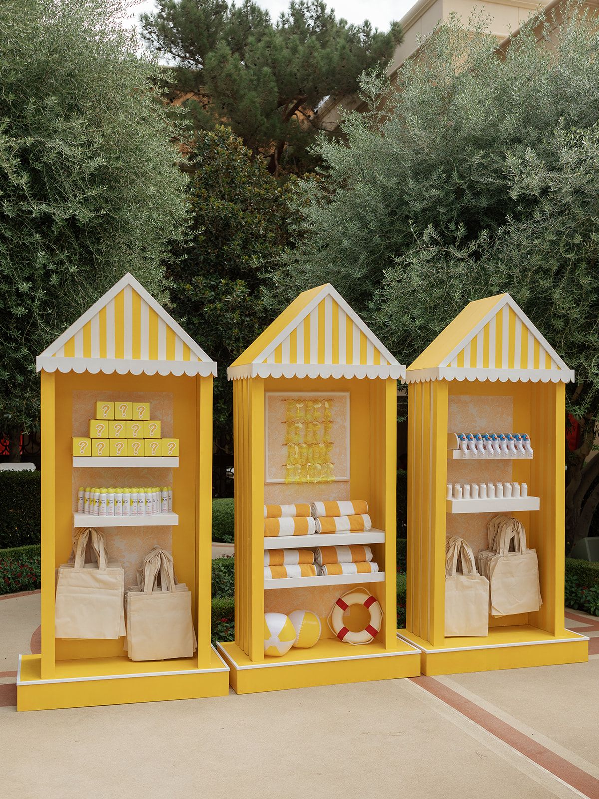 Three yellow and white striped beach cabana display shelves with summer products, tote bags, and a life preserver.