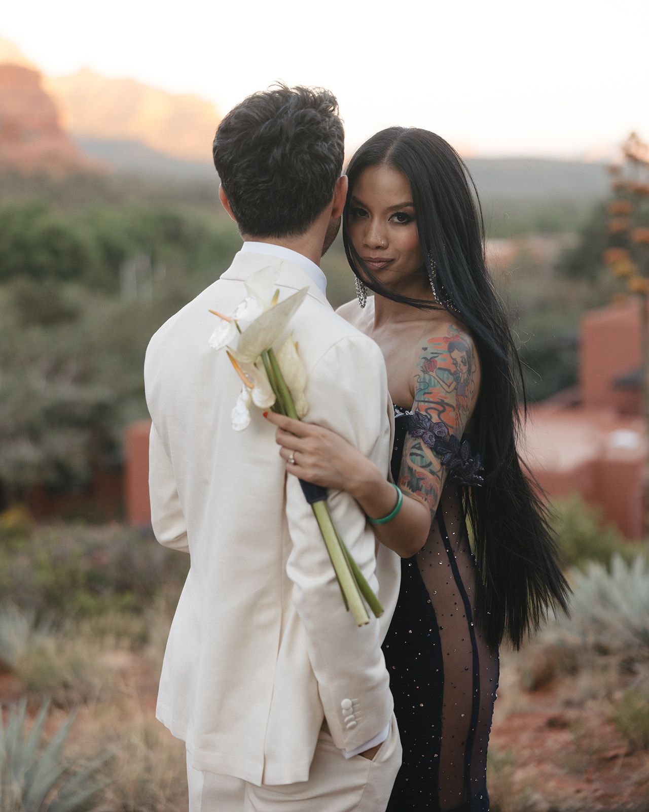 A couple in formal attire sharing an intimate moment at sunset with desert scenery and mountains in the background.