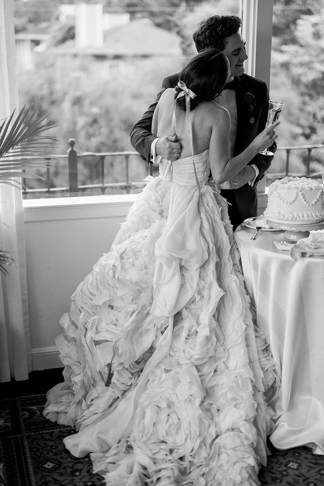 A romantic wedding couple in a white dress and dark suit share an intimate embrace at their reception venue.