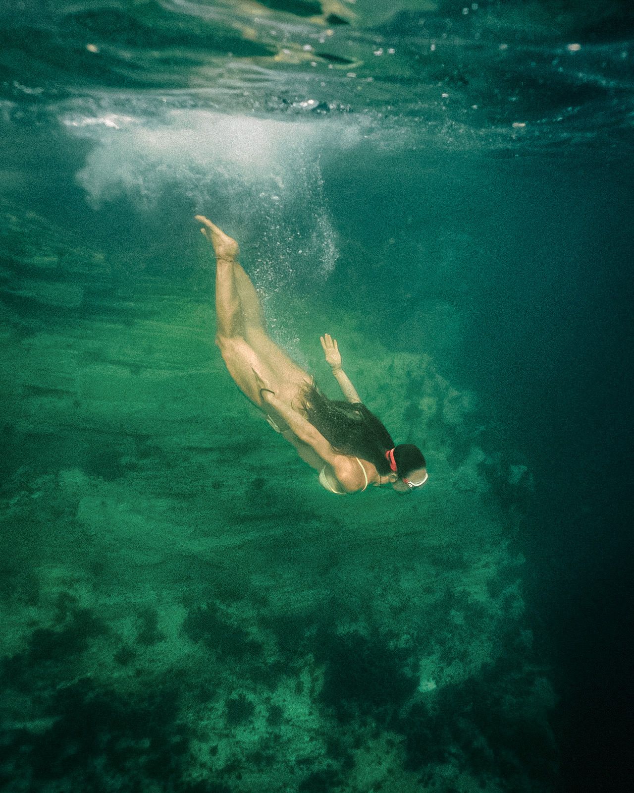 Underwater view of a swimmer diving gracefully through turquoise waters with streaming bubbles and sunlit reflections.