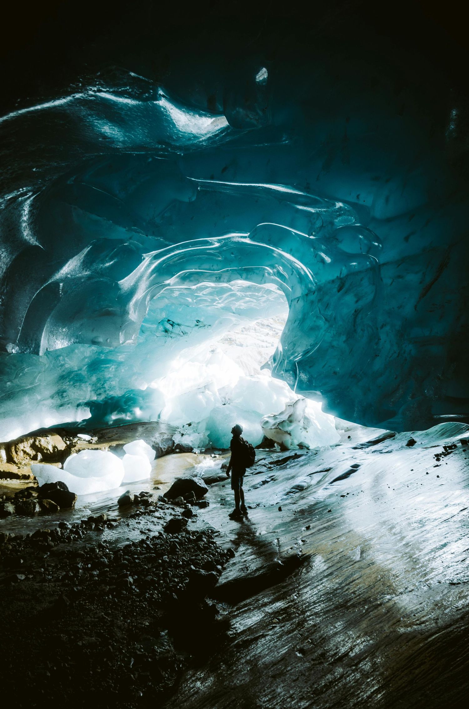 Blue ice cave interior with ethereal lighting and silhouetted figure.