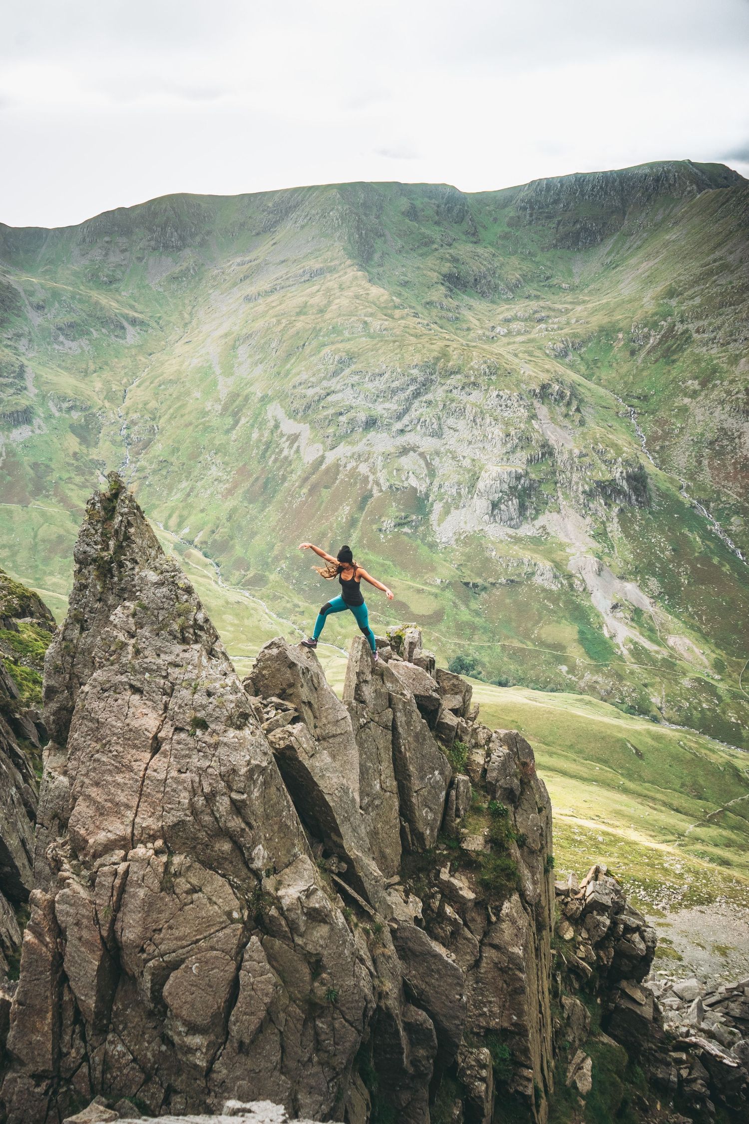 Rock climbers ascend a jagged mountain ridge with dramatic green valleys and peaks in the background.