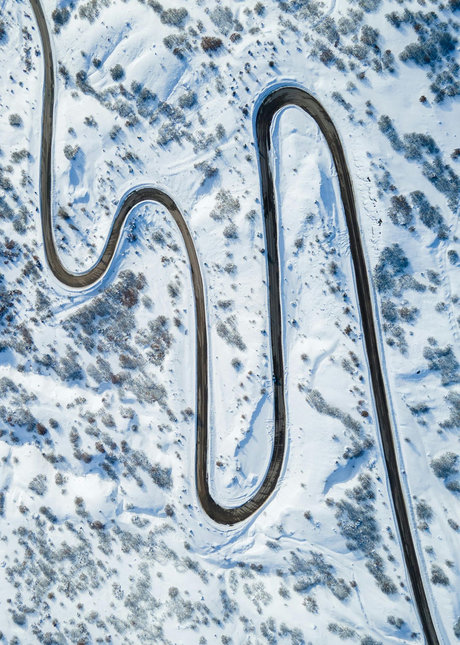 Aerial view of a winding mountain road through snowy winter landscape.