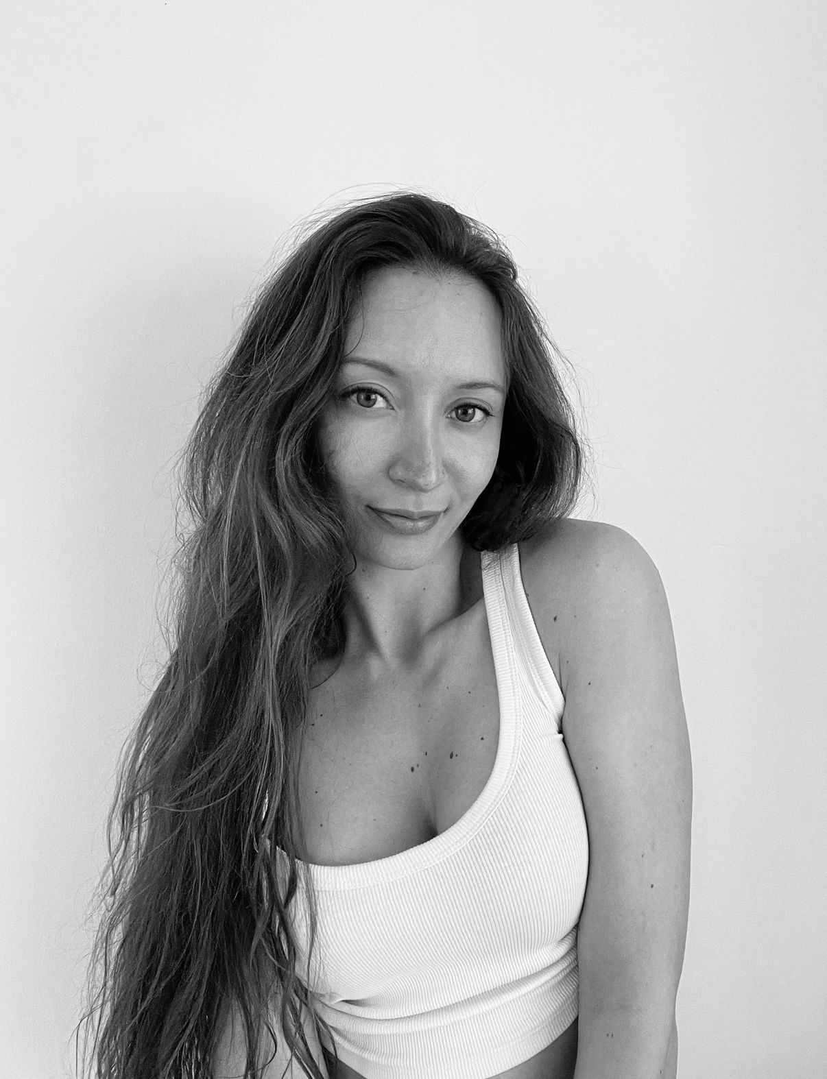 Black and white portrait of someone with long dark hair wearing a white tank top against a light background.