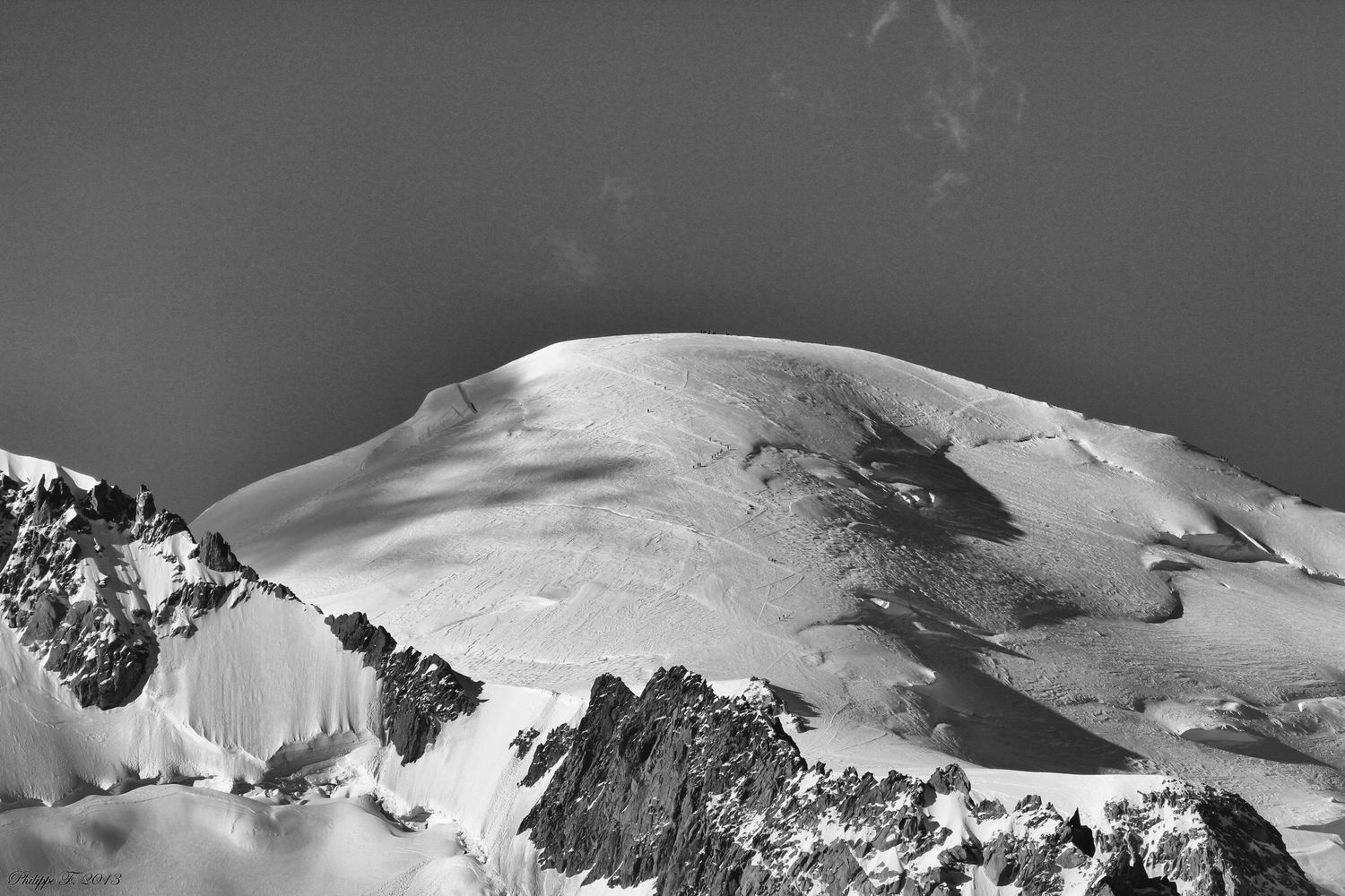 Snow-covered mountain summit in dramatic black and white against dark sky.