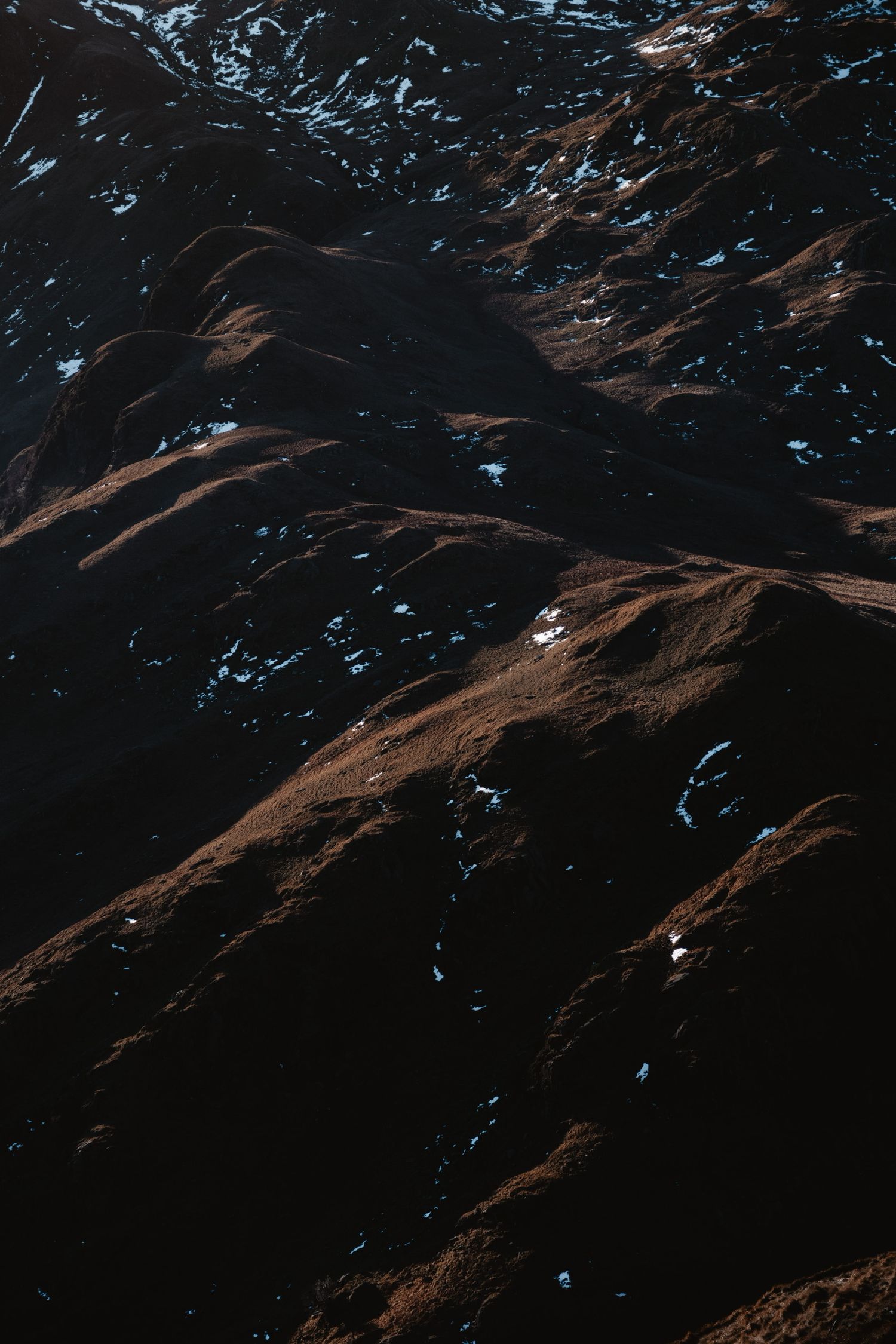 Dark rocky mountain terrain with patches of snow and ice in dramatic lighting.