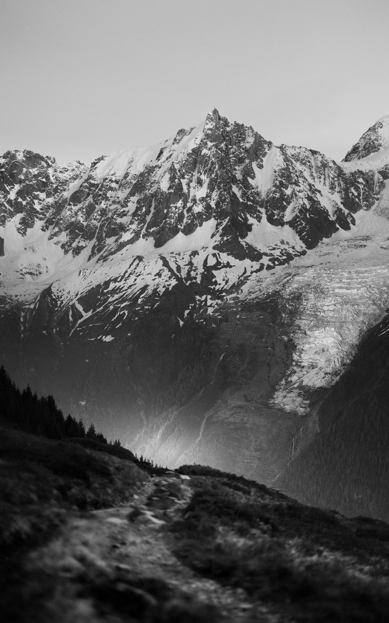 Dramatic black and white mountain peak with snow-covered slopes and rocky terrain in alpine landscape.
