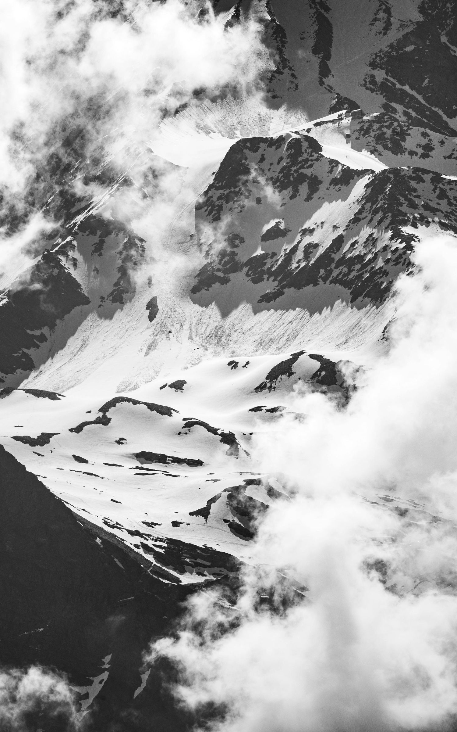 Majestic snow-capped mountain peaks shrouded in swirling clouds captured in black and white.