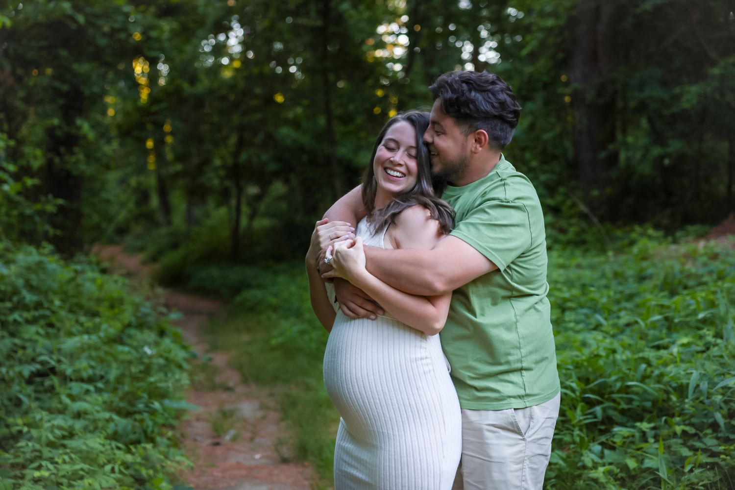 A couple shares an intimate moment embracing on a forest trail surrounded by lush greenery.