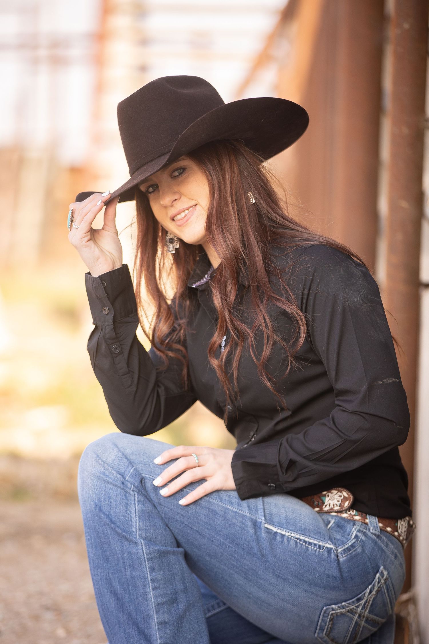 Western style portrait with black hat and shirt against rustic wooden backdrop.