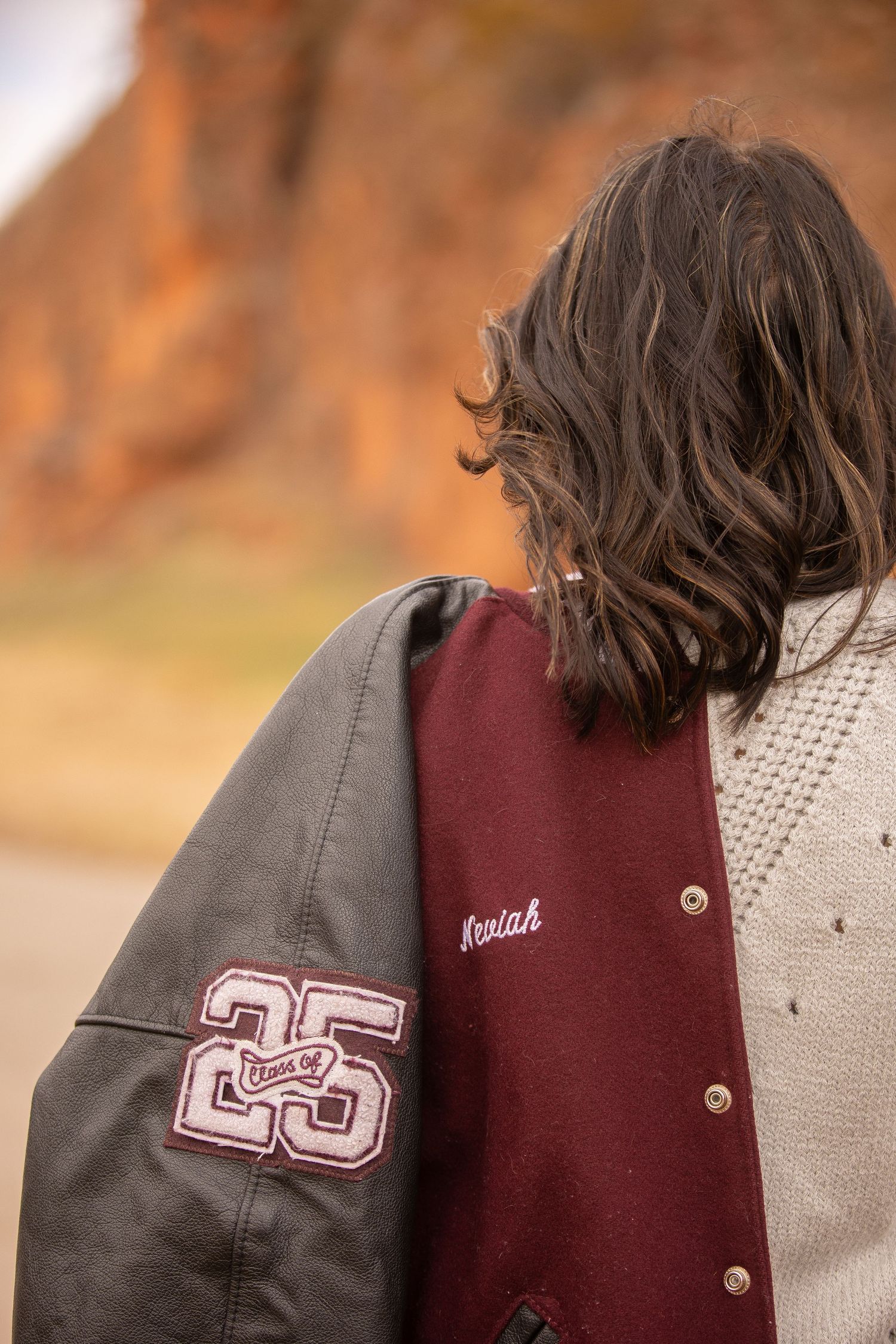 Varsity letterman jacket with number 25 shown from behind against rustic background.