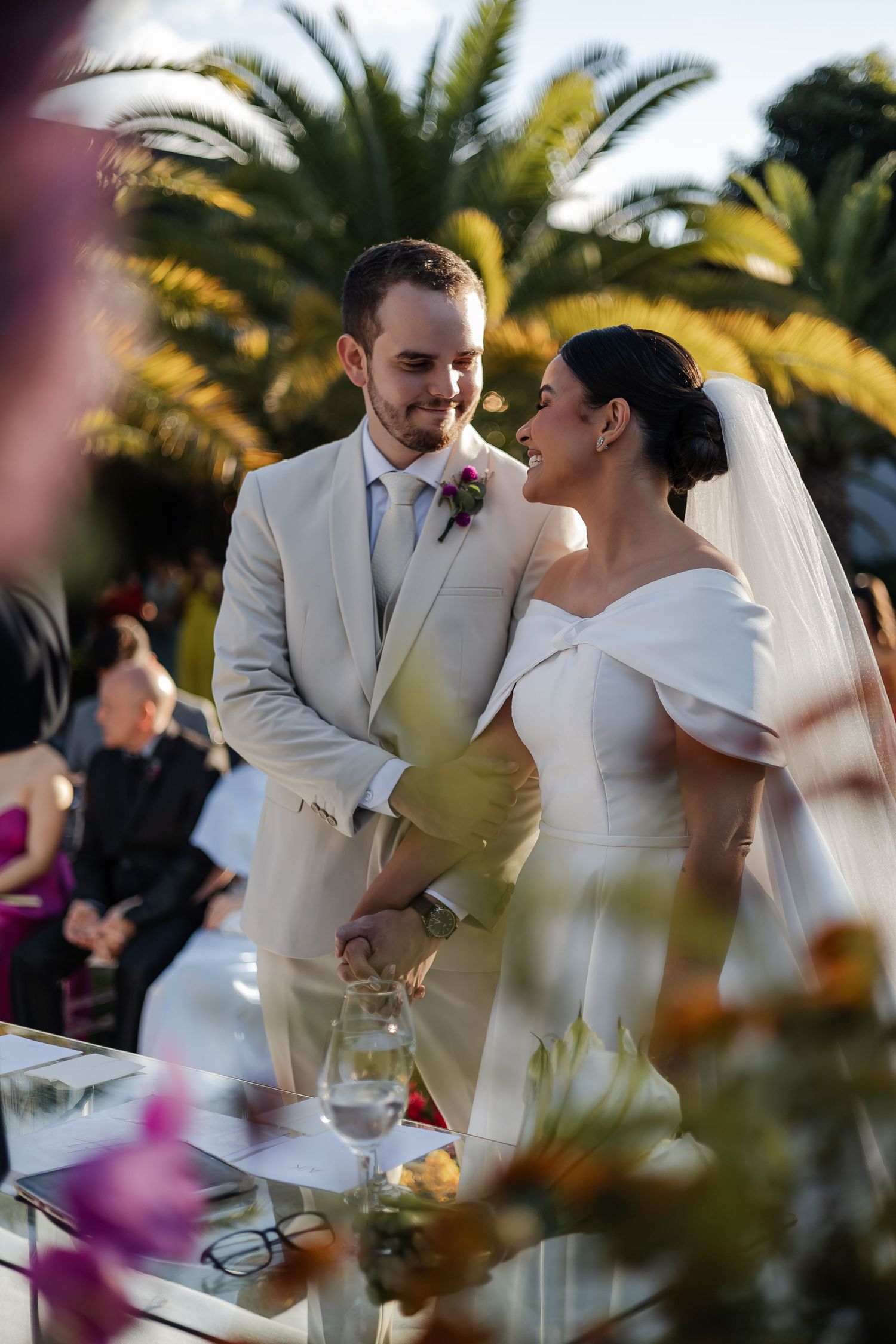 Newlyweds share a tender moment during their tropical outdoor wedding reception with palm trees in the background.
