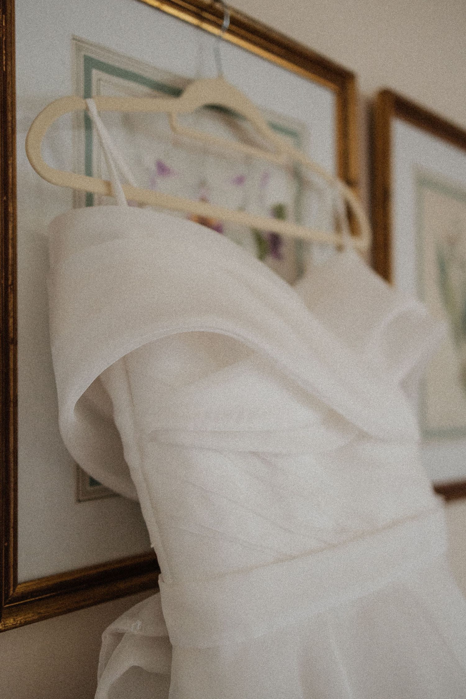 A white wedding dress hangs elegantly on display with its flowing fabric and sweetheart neckline visible against a wall.