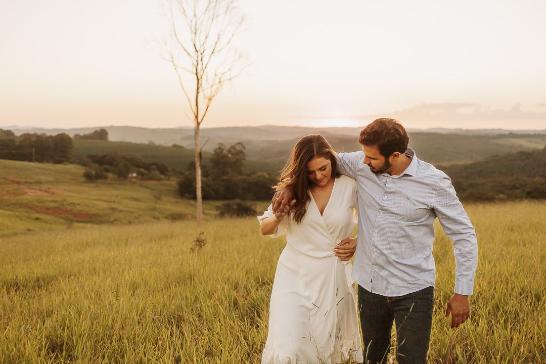 Two people walking together through a golden grassy field at sunset with rolling hills in the background.