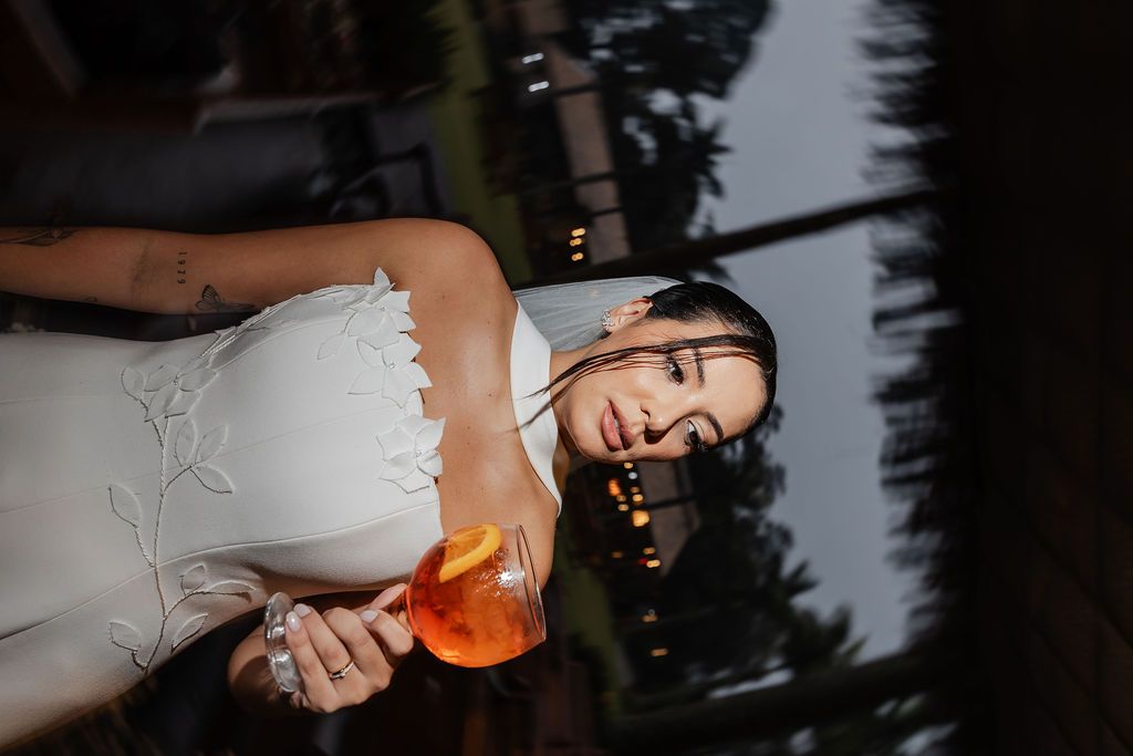 A person in white holds an orange cocktail against a dark evening background.
