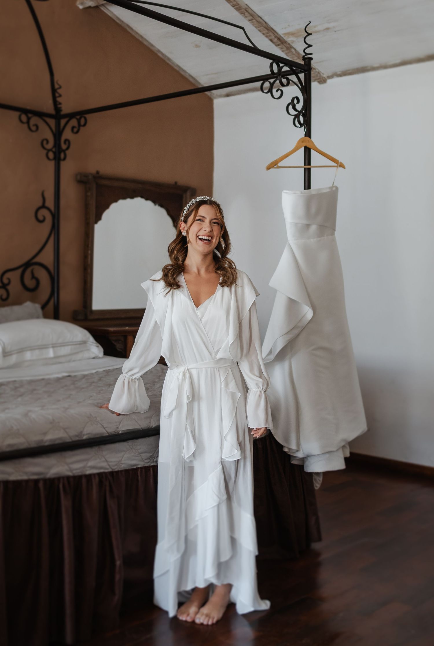 A series of white linen robes and garments hanging from rustic iron hooks against a warm-toned wall in a room.